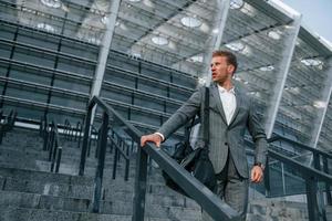 Young businessman in grey formal wear is outdoors in the city photo