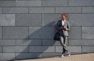 contra la pared gris. un joven hombre de negocios con ropa formal gris está al aire libre en la ciudad foto