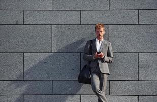 Against grey wall. Young businessman in grey formal wear is outdoors in the city photo