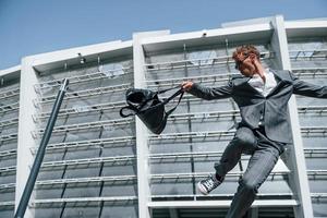 Jumping and celebrating success. Young businessman in grey formal wear is outdoors in the city photo