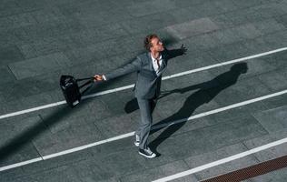 Dancing, celebrating success. Young businessman in grey formal wear is outdoors in the city photo