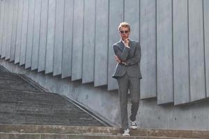 posando para una cámara. un joven hombre de negocios con ropa formal gris está al aire libre en la ciudad foto