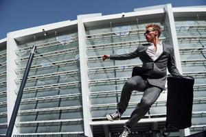 Jumping and celebrating success. Young businessman in grey formal wear is outdoors in the city photo