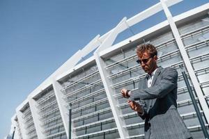 Big stadium behind. Young businessman in grey formal wear is outdoors in the city photo