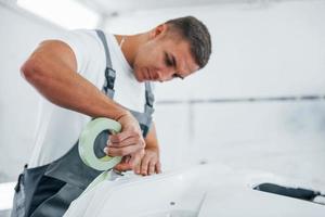 Works with car hood. Caucasian automobile repairman in uniform in garage photo