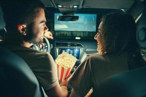 hermosa pareja joven feliz sentada en el auto juntos y comiendo palomitas de maíz foto