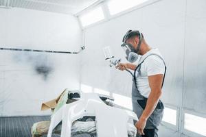 Uses painting gun. Caucasian automobile repairman in uniform works in garage photo