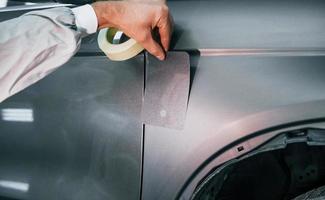 Applying new color. Caucasian automobile repairman in uniform works in garage photo