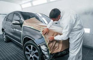 Covering car by brown cloth. Caucasian automobile repairman in uniform works in garage photo