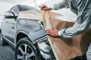 Covering car by brown cloth. Caucasian automobile repairman in uniform works in garage photo