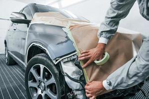 cubriendo el coche con tela marrón. reparador de automóviles caucásico en uniforme trabaja en garaje foto