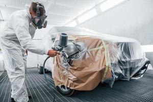 Painting job in progress. Caucasian automobile repairman in uniform works in garage photo