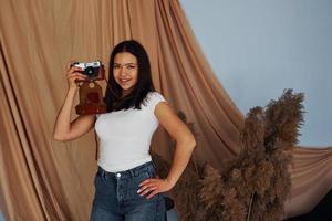 Young cheerful woman holds indoors and holds retro camera photo
