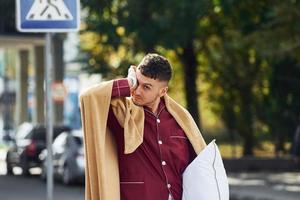 Young man in pajama is outdoors on the street. Feels sleepy photo