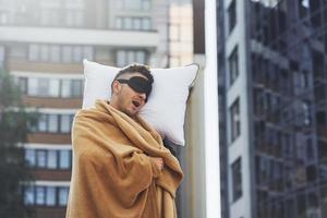 edificio de negocios en segundo plano. joven en pijama está al aire libre en la calle. se siente somnoliento foto