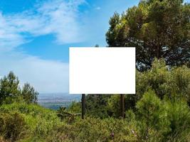 cartelera vacía en una colina con un árbol en un fondo bajo un cielo azul foto