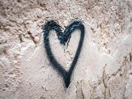 Side view photo of a heart drawn with a black spray paint on an old damaged concrete wall