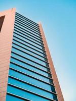 A modern tall building with large windows photographed from below against a blue sky photo