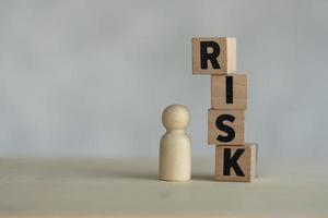 Pile wooden cubes of RISK text placed near wooden figures peg doll, Risk assessment, decision to accept business result in uncertainty. photo