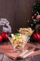 Russian olivier salad of sausage and boiled vegetables in bowls on a wooden table. Vertical view photo