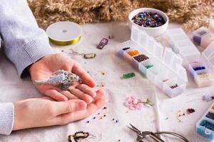 Bird woven from beads in children's hands among boxes with beads photo