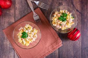 Russian olivier salad of sausage and boiled vegetables in bowls on a wooden table. Top view photo