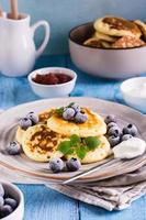 Pancakes with blueberries, sour cream and mint on a plate on the table. Homemade baking. Vertical photo