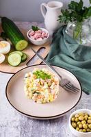 Traditional Russian Olivier salad of boiled vegetables and sausages on a plate. Vertical view photo