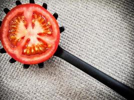 Half tomato on a toothed kitchen spoon on a gray ground. Horizontal image. photo