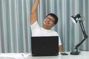 happy businessman looking up and showing winner gesture while sitting at workplace photo