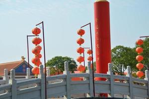 ambos farolillos rojos chinos han escrito un patrón afortunado y chino, la decoración cuelga cerca de un gran pilar rojo con caracteres chinos dorados escritos en el puente del santuario. foto