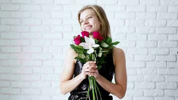 Valentinstag. Junge positive Frau, die Blumen über weißem Backsteinmauerhintergrund riecht video