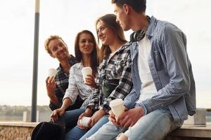 Sunny weather. Drinking coffee. Group of young cheerful friends that is outdoors having fun together photo