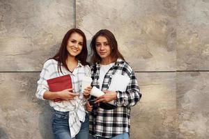 tiene paquete rojo de café. hermosos amigos alegres o una pareja de lesbianas juntos cerca de la pared al aire libre durante el día foto