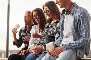 Sunny weather. Drinking coffee. Group of young cheerful friends that is outdoors having fun together photo