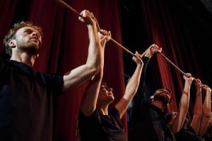 Holding rope in hands above the heads. Group of actors in dark colored clothes on rehearsal in the theater photo