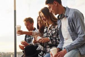 tiempo soleado. bebiendo café. grupo de jóvenes amigos alegres que están al aire libre divirtiéndose juntos foto