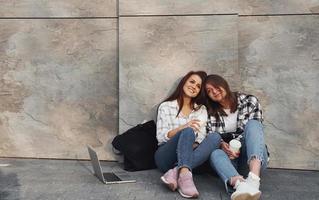 con taza de café. hermosos amigos alegres o una pareja de lesbianas juntos cerca de la pared al aire libre durante el día foto