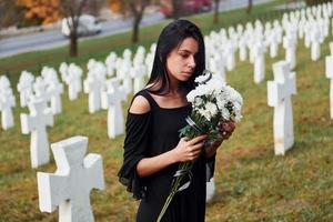 Young woman in black clothes visiting cemetery with many white crosses. Conception of funeral and death photo