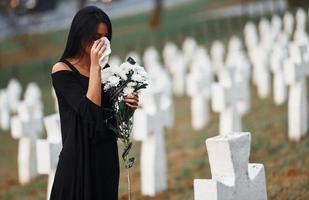 joven vestida de negro visitando el cementerio con muchas cruces blancas. concepción del funeral y la muerte foto
