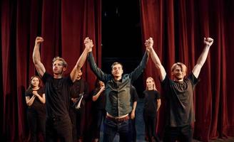 With hands up. Conception of success. Group of actors in dark colored clothes on rehearsal in the theater photo