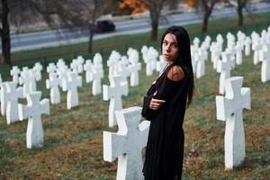 Young woman in black clothes visiting cemetery with many white crosses. Conception of funeral and death photo