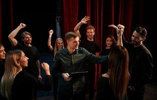 Happy people celebrating success. Group of actors in dark colored clothes on rehearsal in the theater photo