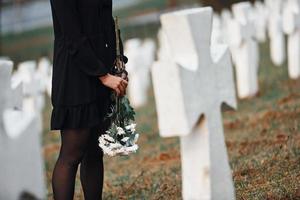 vista de partículas joven vestida de negro visitando el cementerio con muchas cruces blancas. concepción del funeral y la muerte foto