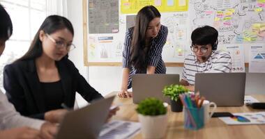 mentor-coach hilft asiatischen männlichen brillenangestellten mit unternehmenssoftware. thailändische kollegen, die beim gruppentreffen gemeinsam an einem projekt arbeiten. besprechen von statistiken, mit laptop, managerberatungskunde. video