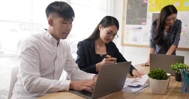 Mentor coach helping asian female glasses employee with corporate software. Thai colleagues working on project together at group meeting. Discussing statistics, using laptop, manager consulting client video