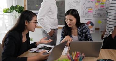 vue latérale d'une femme d'affaires asiatique heureuse qui consulte une collègue à lunettes dans la salle de réunion. entraîneur de mentor féminin joyeux à la négociation. formation de collègue d'entreprise à la salle de conférence. video