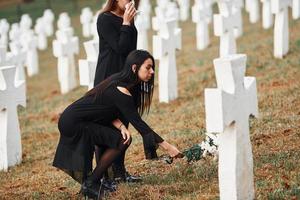 Two young women in black clothes visiting cemetery with many white crosses. Conception of funeral and death photo