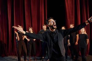 Expressionalible guy practicing his role. Group of actors in dark colored clothes on rehearsal in the theater photo