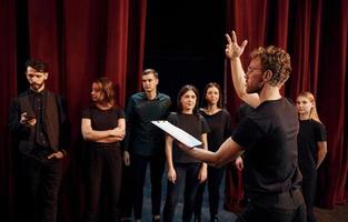 Man with notepad practice his role. Group of actors in dark colored clothes on rehearsal in the theater photo